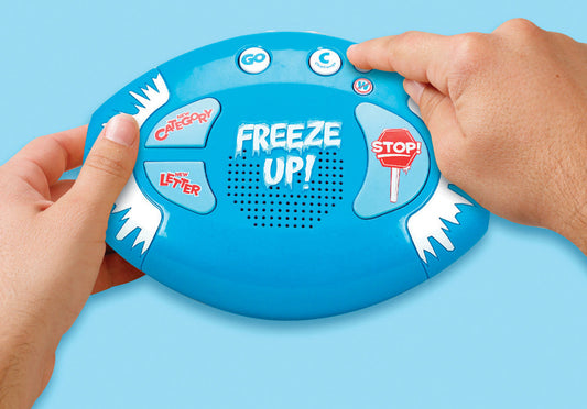 Hands holding a Freeze Up! Electronic Talking Game, a bright blue, oval-shaped electronic talking game with white frosty accents. The game features a large 'Freeze Up!' label in the center above a speaker, with buttons labeled 'New Category,' 'New Letter,' 'Go,' and 'Stop.' The person is interacting with the device, pressing the buttons to play the game