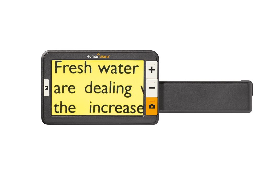 Humanware Explore 5 electronic magnifier which features a high definition LCD screen with physical buttons that include a bright orange camera big button and big gray buttons to increase and decrease size. The device is magnifying an area of text on yellow paper to increase the size to make it easier to read. On the LCD screen is a large magnification. There is a handle coming off the device to the right.